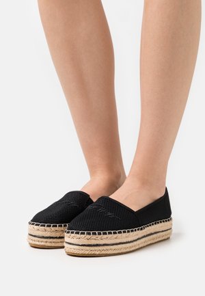 Zapatos espadrilles negros con textura trenzada, que cuentan con una plataforma de yute y detalles en negro. Diseño de punta redonda con detalles elásticos.