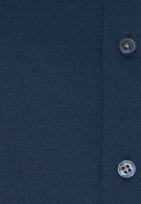 Marineblauwe stof met een gestructureerde weving. Voorzien van een knoopsluiting met een ronde grijze knoop, waardoor een subtiel patroon zichtbaar wordt.