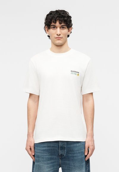 Νέος άνδρας με κοντά σγουρά μαλλιά, που φοράει λευκό T-shirt Barrow με κείμενο και emoji στο στήθος, συνδυασμένο με μπλε τζιν.
