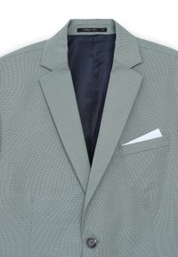 Blazer grigio a fantasia con rever a punta, chiusura con un bottone e taschino sul petto contenente un fazzoletto bianco. L'interno è blu navy.