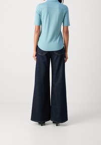 Polo a maniche corte azzurro chiaro con orlo curvato abbinato a pantaloni in denim a gamba larga blu scuro con cuciture a contrasto e tasche posteriori.