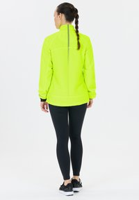 Bright yellow athletic jacket with a high collar, zipper, and reflective accents; paired with black leggings and sporty shoes.