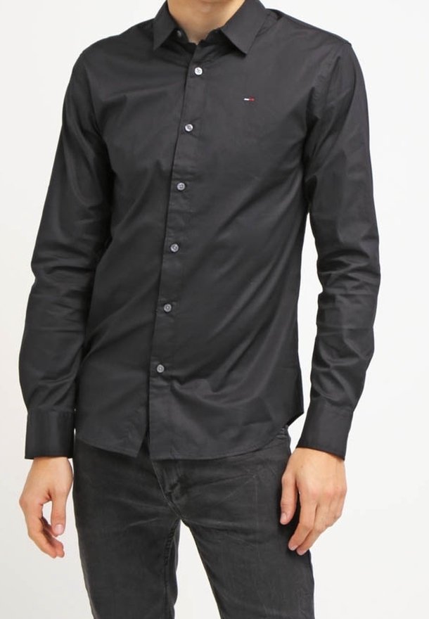 Camisa negra de manga larga con botones y corte entallado, que presenta un logo sutil en el pecho. Textura suave, cuello clásico y puños estándar.
