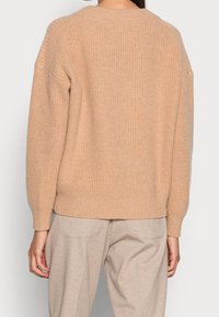Beige pletený svetr s ribovanou texturou, s kulatým výstřihem a designem s klesajícími rameny. Měkký materiál s volným střihem.