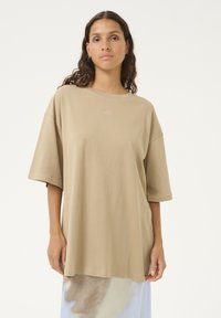 Lockere, kurzärmelige T-Shirt aus beigem Baumwollmaterial mit Rundhalsausschnitt. Verfügt über ein dezentes gesticktes Logo auf der Brust und eine glatte Oberfläche.