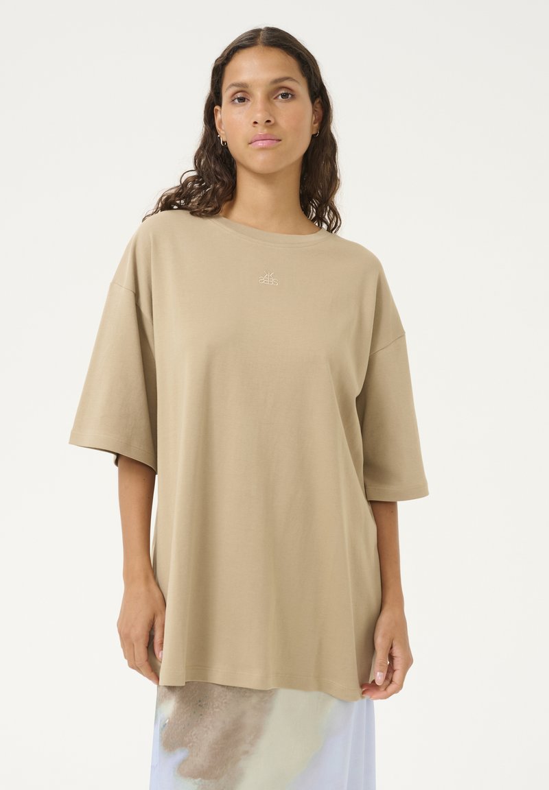 T-shirt in cotone beige a maniche corte e vestibilità ampia, con collo rotondo. Presenta un logo ricamato discreto sul petto e una texture liscia.