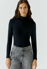 Schwarzes langärmliges Rollkragenoberteil aus glattem Stoff, kombiniert mit hellgrauen, hoch taillierten Jeans mit einem dezenten, ausgewaschenen Muster.