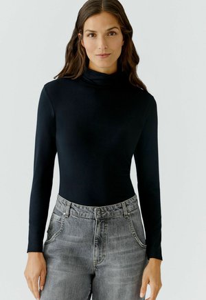 Schwarzes langärmliges Rollkragenoberteil aus glattem Stoff, kombiniert mit hellgrauen, hoch taillierten Jeans mit einem dezenten, ausgewaschenen Muster.