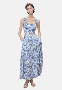 Tvådelad outfit med en cropped top med fyrkantig halsringning och en flödande, golvlång kjol. Tyget är lätt och har ett blått blommönster på en vit bakgrund.