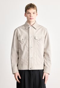 Bézs színű velúr dzseki galléros nyakkivágással, elöl patentos gombokkal és két mellzsebbel. Sima textúra és testre szabott szabás.