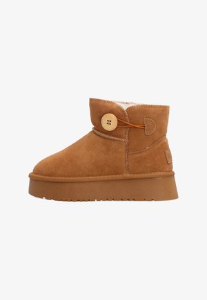 Hnědá semišová kotníková bota s tlustou gumovou podešví, dřevěným knoflíkem, elastickou smyčkou jako zapínáním a fleecovou podšívkou viditelnou na horním okraji.