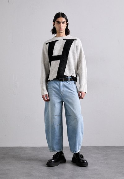 Szürke kötött pulóver nagy fekete "H" betűvel, világoskék, bő szárú farmernadrággal, amely varrási részletekkel rendelkezik. Fekete platform cipők egészítik ki a megjelenést.