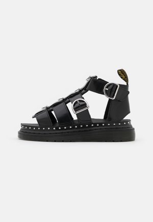 Sort læder gladiatorsandal med sølvspænder, nittet sålkant, tyk gummisål og mærket trækstrop ved hælen.