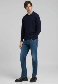 Maglietta a maniche lunghe blu navy con scollo rotondo, abbinata a jeans blu e stivaletti neri robusti. Design semplice senza motivi o loghi evidenti.