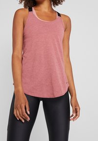 Débardeur de sport rose avec un col arrondi et des bretelles noires, doté d'un tissu doux et texturé et d'un ourlet incurvé. Leggings noirs portés en dessous.