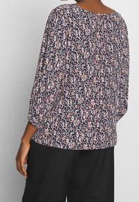 Blouse florale sur fond marine, avec des motifs blancs et corail, encolure ronde et manches trois-quarts avec des accents froncés.