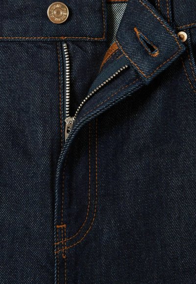 Tela de mezclilla azul marino con costuras naranjas en contraste. Un zipper plateado está parcialmente abierto, revelando un forro interior azul.