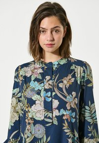 Navyblaues Blumenkleid mit lockerer Passform, das in hellen Farben blüht, mit geknöpftem Einsatz und umgeschlagenen Ärmeln. Glatte Stofftextur.