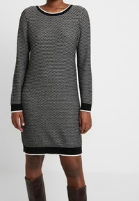 Abito maglione a maniche lunghe in bianco e nero con motivo a strisce, scollo rotondo e bordi e polsini a coste neri a contrasto.