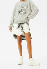 Šedá mikina s potiskem "Virginia", kombinovaná s bílou zavinovací sukní s pruhovaným lemem a mašlí, doplněná bílými teniskami.