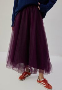 Gonna di tulle viola con vita arricciata, texture a strati, abbinata a sneakers arancioni e bianche. Maglione blu scuro.