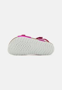 Valkoinen pohja, jossa on sahalaitakuviota ja ilmaventtiilireikiä vaaleanpunaisissa sandaalihihnoissa, kuvattuna pohjasta yksinkertaista taustaa vasten.