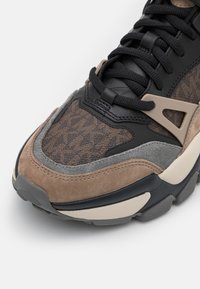 Sneaker med en overdel i blandede materialer i brune og sorte toner, med teksturert stoff, glatt lær og grå semsket skinndetaljer.