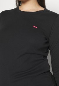 Schwarzes Langarm-T-Shirt aus Baumwolle mit rundem Halsausschnitt. Verfügt über ein kleines rotes Levi's-Logo auf der Brust. Glatte Textur.