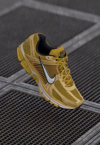 Baskets de course Nike jaunes avec un dessus en mesh, accents noirs et un logo blanc ; présente un design texturé et une semelle en caoutchouc pour l'adhérence.