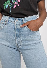 Ljusblå högmidjade jeans i denim, med knappstängning fram, sidofickor och subtila blekningar. Slät textur och klassisk design.