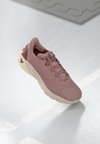 Zapatilla deportiva de un rosa claro con parte superior texturizada, punta suave y suela crema en contraste; incluye perforaciones y una pestaña en el talón.