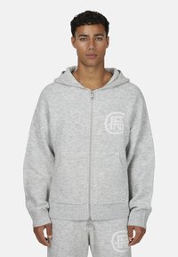 Szara rozpinana bluza z kapturem wykonana z miękkiego materiału, wyposażona w przednią kieszeń, ściągacze na rękawach oraz logo nadrukowane na lewej piersi.