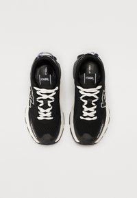 Black athletic sneakers with mesh upper, white laces, and contrasting midsole. Features logo detail on side and back heel.