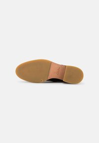 Semelle de chaussure noire en cuir et caoutchouc. Présente une forme arrondie et une texture lisse ; accents marron clair près du talon.
