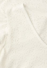 Tissu blanc avec un motif texturé de petits trous et un détail d'encolure en forme de V.