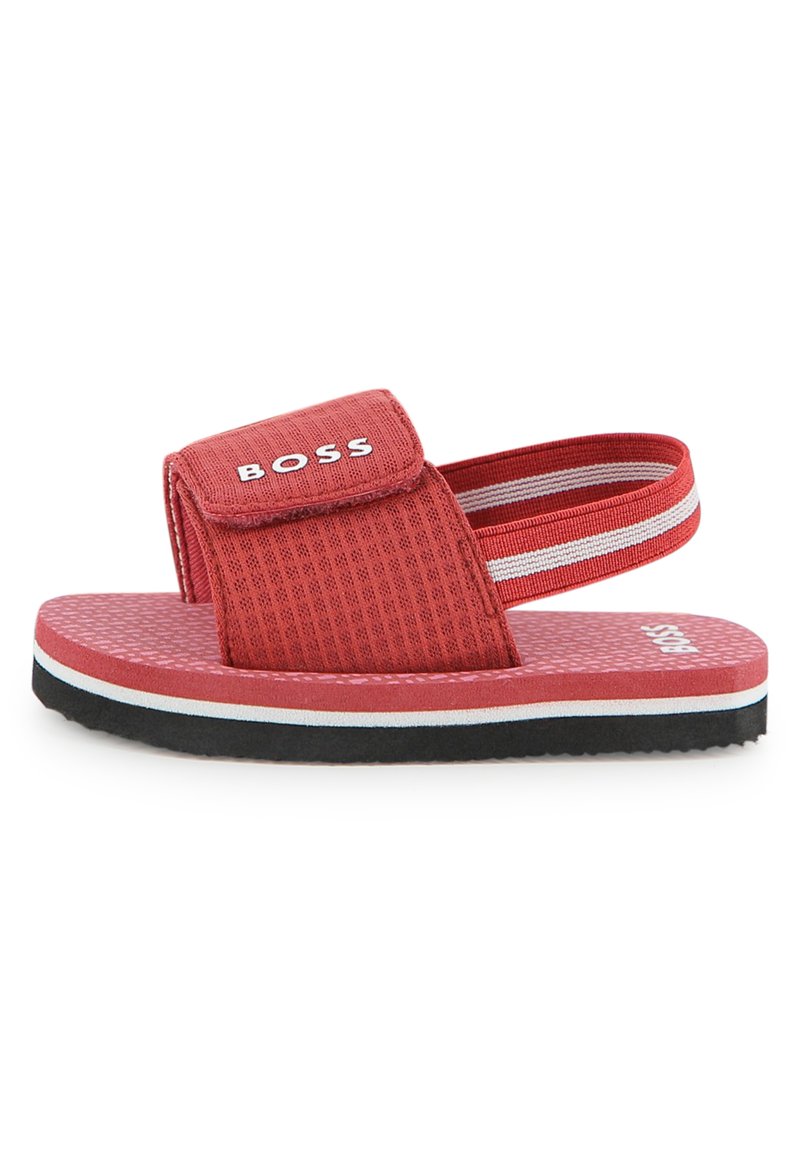 Κόκκινο σανδάλι με υφασμένο επάνω μέρος και λουράκι βέλκρο, που διαθέτει λευκή και μαύρη σόλα με μπλε λεπτομέρειες και σχέδιο με τελείες στο πέλμα.