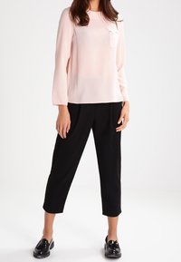 Light pink long-sleeve top with a pocket and black cropped trousers. The outfit features smooth textures and black glossy shoes.