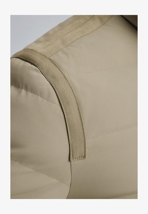 Chaqueta acolchada beige con hombros que presentan una correa texturizada y un diseño acolchado. Exterior liso con sutiles acentos de costura.