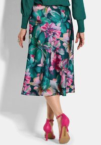 Jupe midi florale ornée de grandes fleurs roses et vertes sur fond bleu-vert foncé. Assortie avec des chaussures à talons hauts roses.