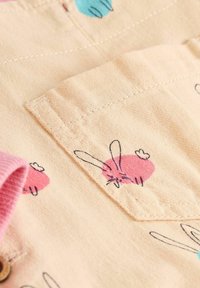 Jasnobeżowa tkanina z małymi, zabawnymi ilustracjami królików w różowym i niebieskim kolorze. Zawiera różowy kołnierz oraz detal kieszonki z przodu.