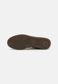 Brūna gumijas sporta apavu zole ar faktūras rakstu, kurā ir apļveida akcenti un viļņveida līnijas. Adidas logo redzams tuvu papēžam.