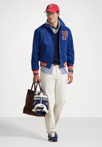 Blue corduroy jacket with red and white stripes, white shirt with blue stripes, cream pants, brown bag, and navy sneakers. Red cap with logo.