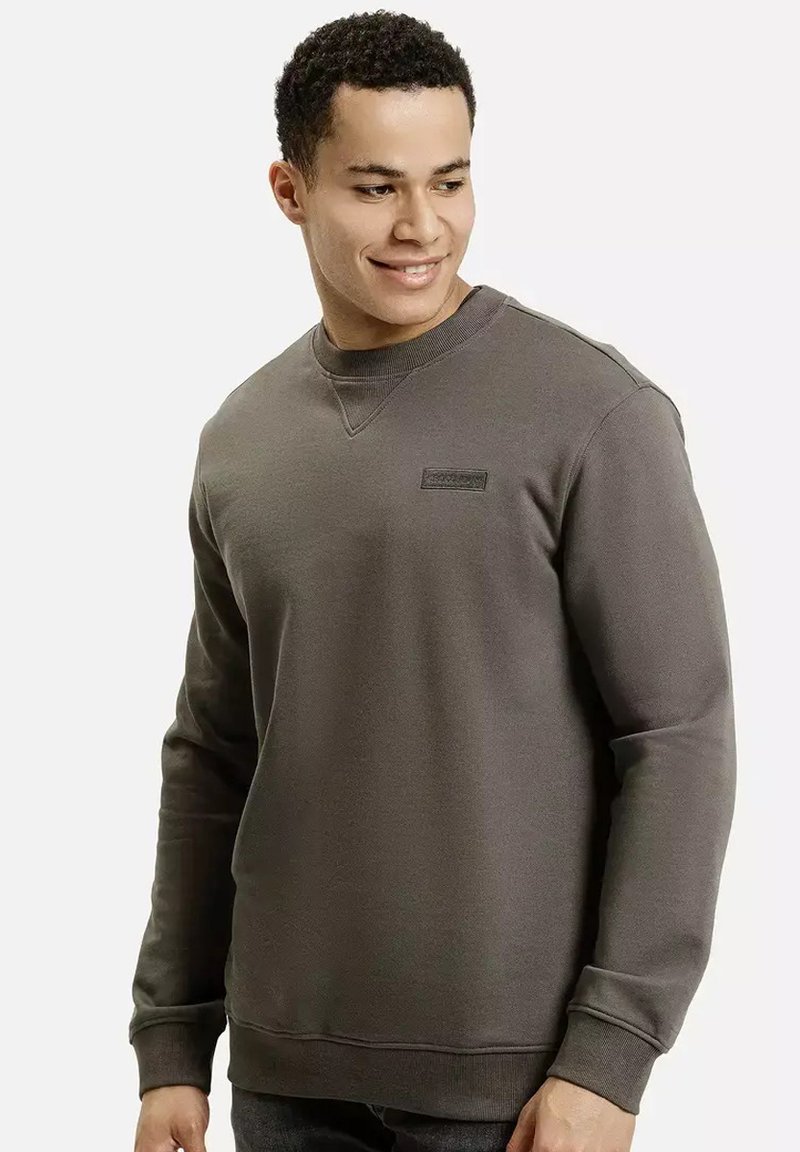 Szara bluza z okrągłym dekoltem, długimi rękawami i subtelną naszywką z logo na piersi. Materiał wydaje się miękki i teksturowany.