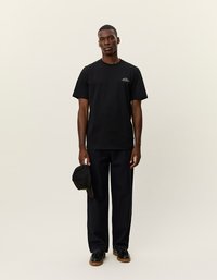 Čierne bavlnené tričko s okrúhlym výstrihom, spojené s tmavomodrými nohavicami. Obsahuje malé logo na hrudi. Nosené s čiernym čiapkou.