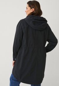 Zwarte hooded jacket met een getailleerde taille, knoopdetails op de manchetten en een relaxte pasvorm, gemaakt van een soepele, lichte stof.
