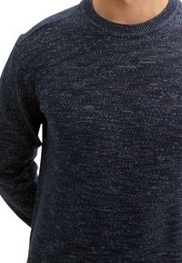Pull en maille marine avec un motif texturé et multi-tons. Il présente un col rond et des manches longues, fabriqué en tissu doux et extensible.