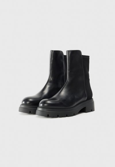 Botas de tobillo de cuero negro con un diseño elegante, puntera redondeada, paneles laterales elásticos y una suela de goma gruesa con patrones de tracción.