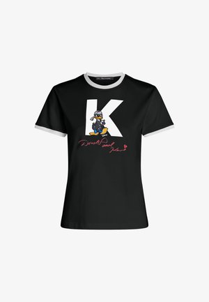 Melnas kokvilnas t-krekls ar kontrastējošu pelēku ribotu apkakli. Uz tā ir liela balta burta "K" un izšuvums ar Džona Duka grafiku, kam pievienots rozā teksts.