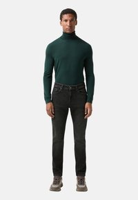 Zelený rolák, úzké černé džíny a šedé tenisky. Rolák je z měkké pleteniny; džíny mají jemné vyblednutí; boty mají strukturované detaily.