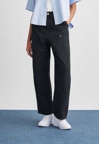 Μαύρο τζιν με φαρδιά παντελόνια, εμπρόσθιες τσέπες, ασημένια κουμπιά και λεία υφή. Συνδυασμένο με ανοιχτό μπλε κοντομάνικο πουκάμισο και λευκά παπούτσια.